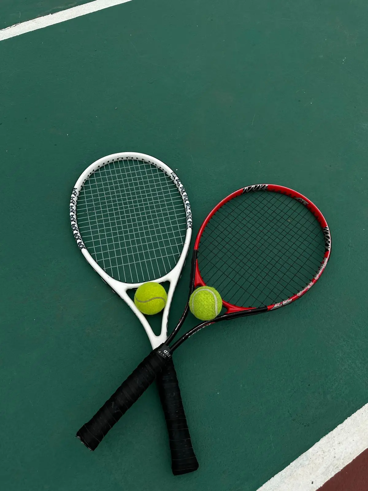 Two tennis rackets and balls on a hard court